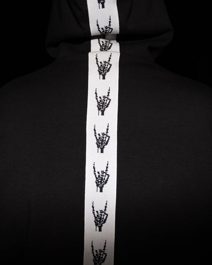 A black hoodie featuring a prominent white vertical stripe down the center, decorated with a repeating black graphic of skeletal hands making the rock on gesture.